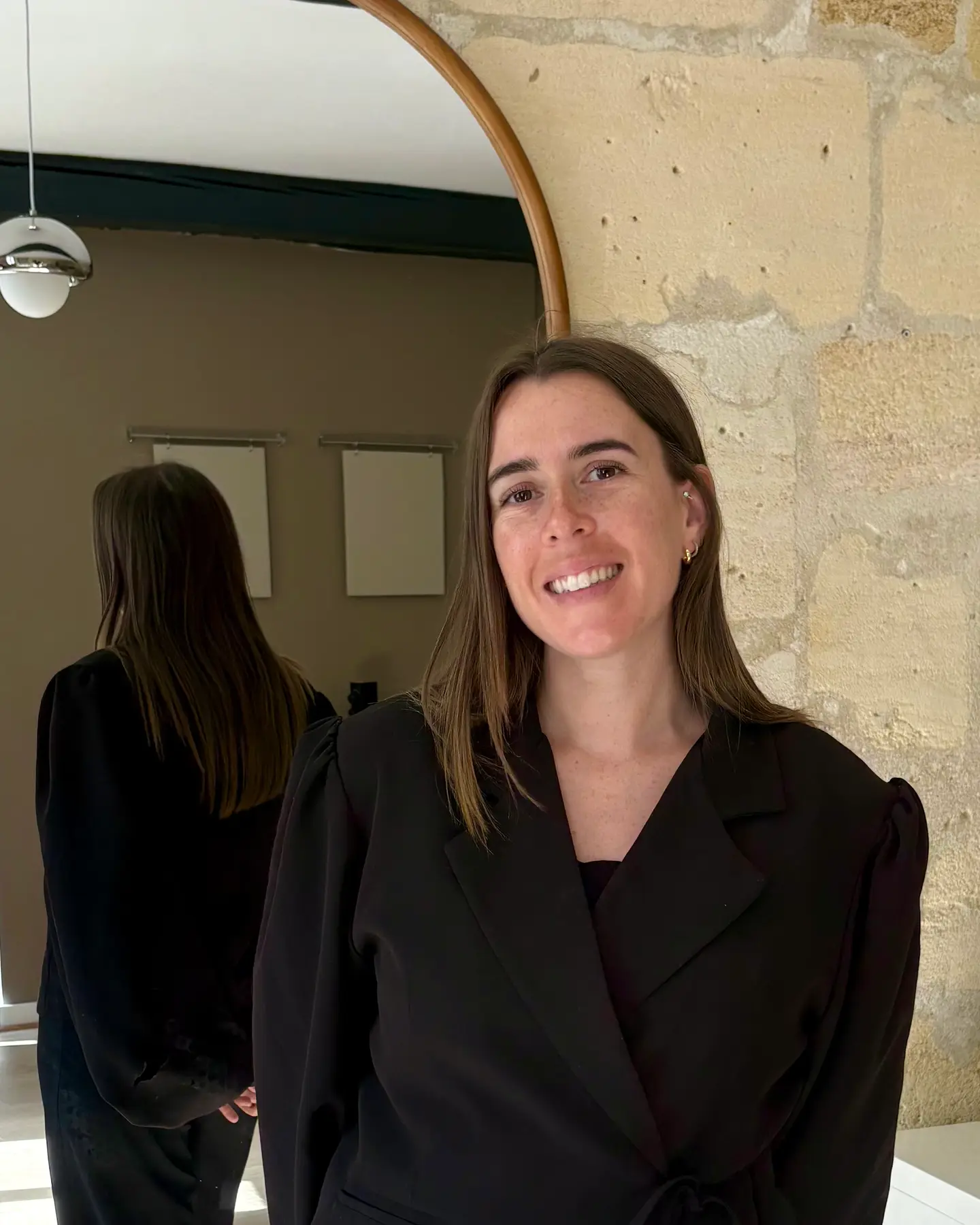 Portrait de Mylène souriante dans son institut, mur en pierre en fond